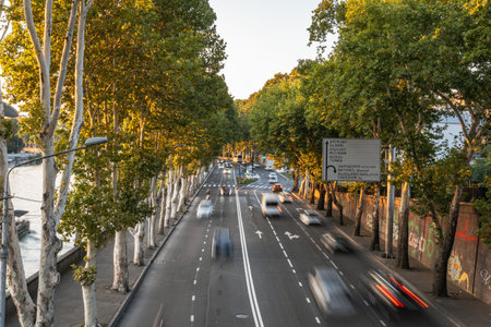 A long exposure photo of a bustling street with blurred cars, a river, and a sign under a warm evening sky.の写真素材