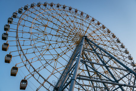 A large Ferris wheel with numerous passenger cabins and intricate metal supports against a clear blue sky.の写真素材