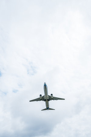 A large passenger jet with its landing gear extended, seen from below, flying in a cloudy sky.の写真素材