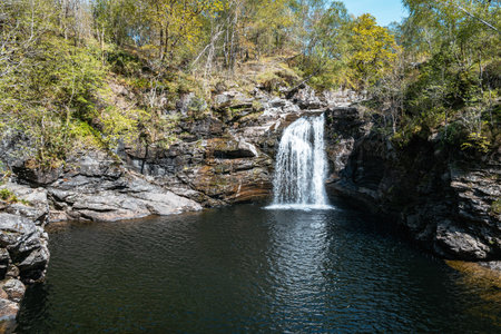 A scenic view of the beautiful Falls of Falloch waterfall in the Loch Lomond The Trossachs National Park, Scotland, surrounded by rich green and yellow foliage.の写真素材