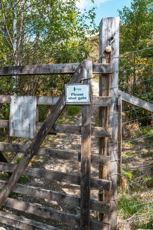 A weathered wooden gate with a small white sign reading Please shut gate on a public footpath in a...