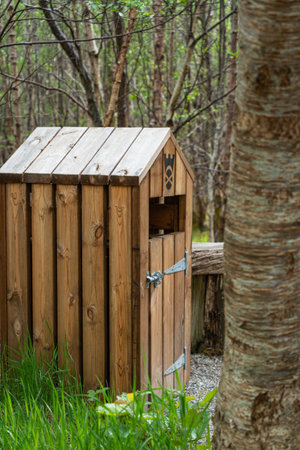 A rustic wooden litter bin sits on a gravel path in a lush green forest, offering a waste solution...