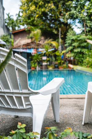 A white plastic lounge chair sits on a concrete pool deck next to a clear blue swimming pool in a...