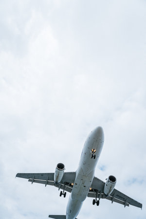 Commercial airliner flying with landing gear down against a cloudy skyの写真素材