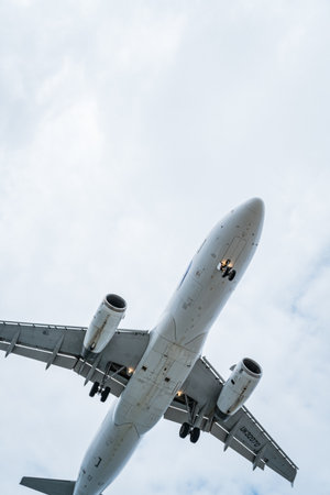 Commercial airliner flying with landing gear down against a cloudy skyの写真素材