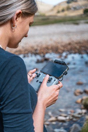 A close-up vertical photo of a woman holding and operating a gray remote controller with her...