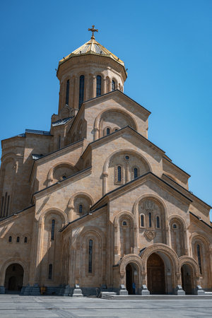 A bell tower building with arches and a cross in the garden of the Holy Trinity Cathedral with a...