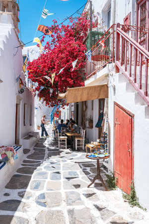 A man stands barefoot next to a Mykonos lifeguard station, with yachts in the harbor and a clear blue sea and sky on a summer day.の写真素材