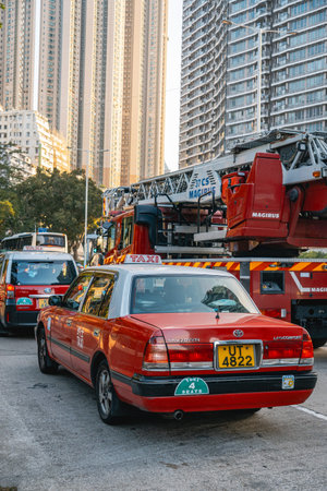 Iconic red cab driving next to large fire truck on urban road in Kowloon