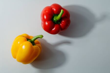 Two bell peppers with green stem on gray background with shadows and copy space