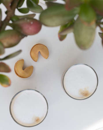 Two Glasses of coffee with cream and two fortune cookies near the leaves on white background. High...