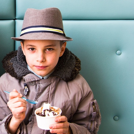 Cute teenage boy eating ice cream with chocolate topping in cafeの写真素材