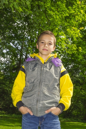 Cute  boy in a yellow hoodie against green tree backgroundの写真素材