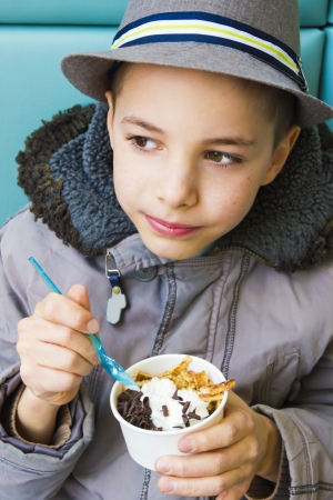 Cute teenage boy eating ice cream with chocolate toppingの写真素材