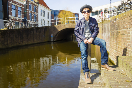 Cute teenage boy in hat (full-length portrait) against canal backgroundの写真素材