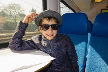 Handsome boy with sunglasses rides on a train reading from the paperの写真素材