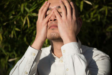 Relieved young man covering face with hand while standing against bamboo backgroundの写真素材