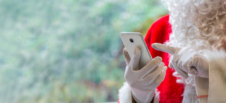 Santa Claus holding mobile phone ready for Christmas time on background. The season, winter, holiday, celebration, gift conceptの写真素材