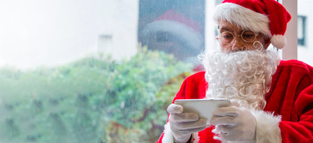 Santa Claus holding mobile phone ready for Christmas time on background. The season, winter, holiday, celebration, gift conceptの写真素材