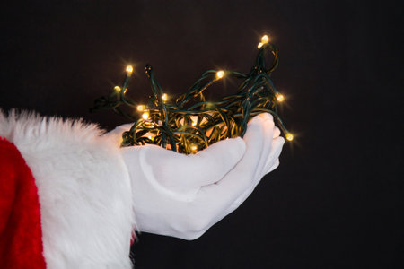 Santa Claus hand holding christmas lights on backgroundの写真素材