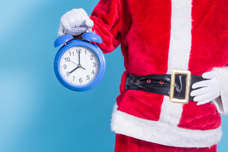 Santa Claus holding alarm clock on blue background, Christmas arrival concept