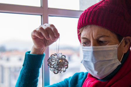 senior woman with disposable surgical mask placing christmas decorationsの写真素材