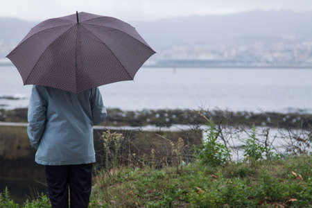 woman with umbrella walking along the coastの写真素材