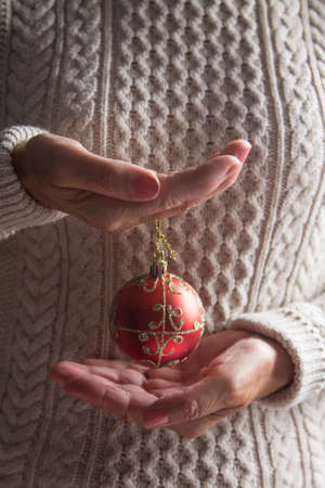 Christmas ball decor in women hand. Christmas greeting card. Woman's hands hold christmas or new year decorated gift.の写真素材