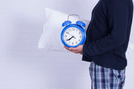 man in pajamas with pillow in hands and alarm clock