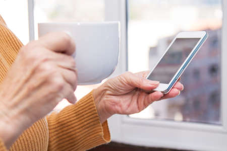 senior woman having a cup of coffee and using mobile phoneの写真素材