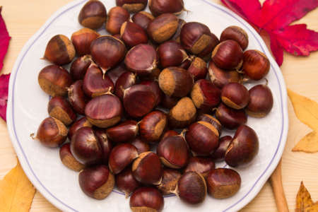 plate of chestnuts on wood and dried leavesの写真素材