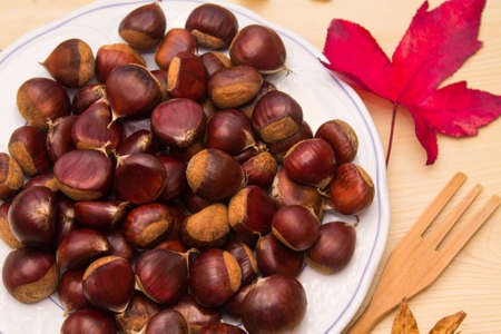 plate of chestnuts on wood and dried leavesの写真素材