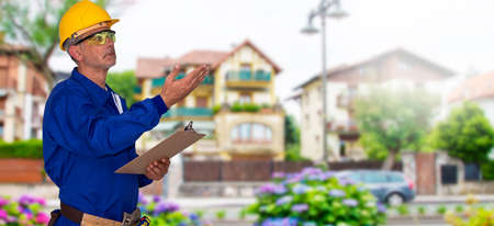 builder or senior mason with blueprints and tools with houses backgroundの写真素材