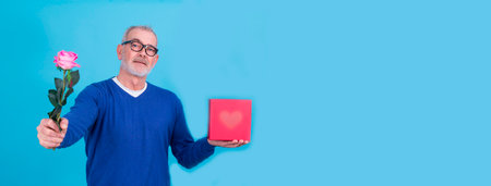 attractive senior man with gift box and flower. birthday or valentines day conceptの写真素材