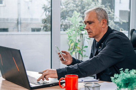businessman in office with phone and using computerの写真素材