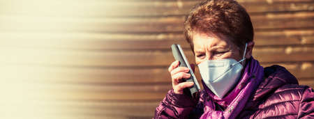 senior woman using mobile phone with mask and disposable medical gloves. Safety measures during the coronavirus outbreakの写真素材