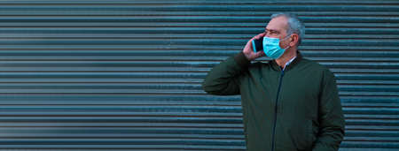 adult man with medical mask talking with mobile phone on gray blind backgroundの写真素材