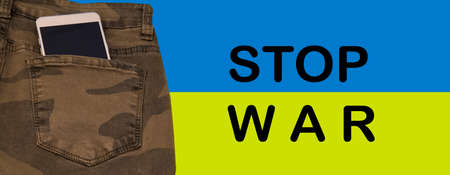 ukraine flag with military jeans, smart phone and anti war protest message. invasion, army soldier,...