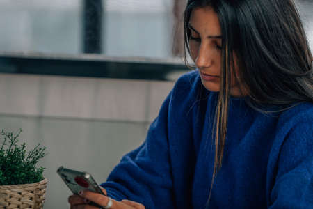 young hispanic latin woman in coffee shop using mobile phoneの写真素材