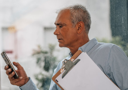 mature man with documents using mobile phone at the windowの写真素材
