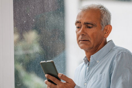 mature man using mobile phone at the windowの写真素材