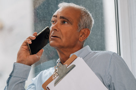 mature man with documents using mobile phone at the windowの写真素材