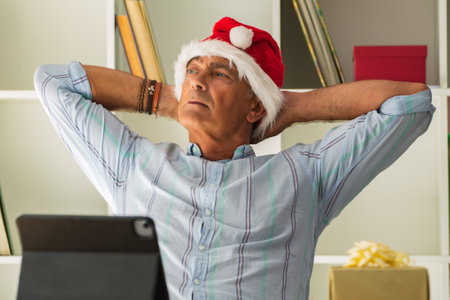 mature man with santa claus hat relaxed and happy at office or workplace