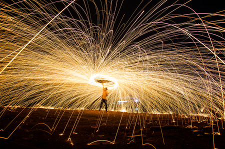 Fire dancing steel wool on the rock coast in the twilight.