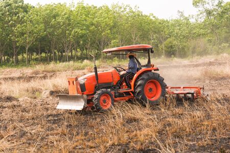 Farmer plowing stubble field with orange tractorの写真素材