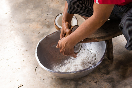 Woman sit on coconut grater and grate coconut into bowlの写真素材