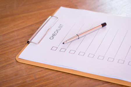 Checklist concept - checklist, paper and a pen with checklist word on wooden tableの写真素材
