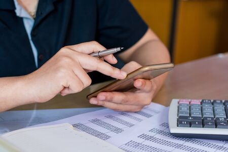 close up hand woman calculating about cost and using smartphone searching data in office.の写真素材