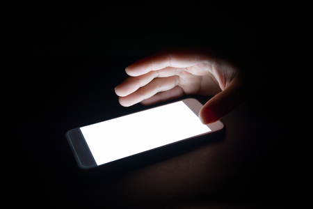 white light from the smartphone reflect your hand at night in the dark.blank screen for text and designの写真素材