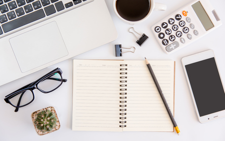 White office desk table, workspace office with laptop, smartphone black screen, coffee cup,pen,calculator, glasses, Top view with copy spaceの写真素材
